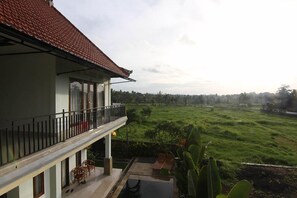A two-story building with a balcony, a swimming pool, and a view of a green field. - Balibbu Ubud Villa (Ubud)
