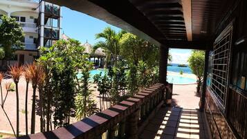 Vista de un área de piscina con terraza de madera y plantas tropicales, que da a una playa con una vista despejada del océano.