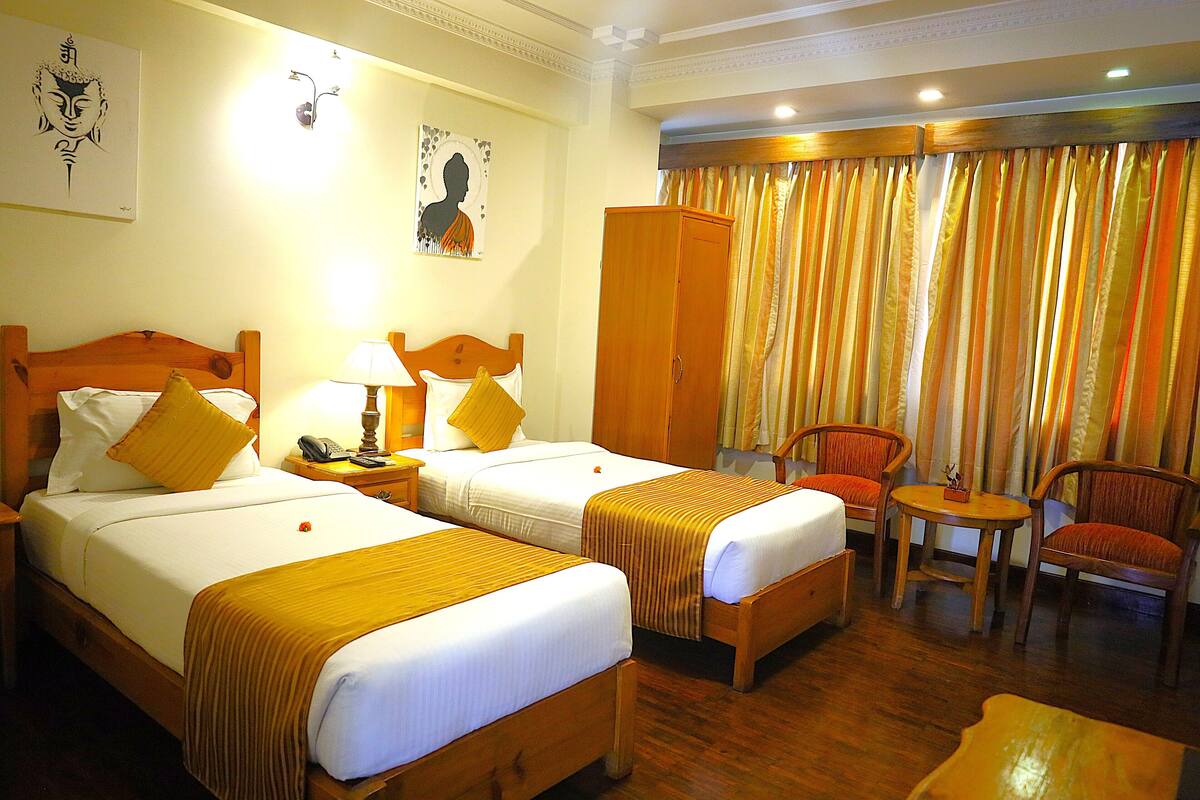 Une chambre d’hôtel avec deux lits, une armoire, une petite table, deux chaises et un rideau.