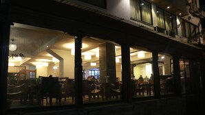 A dimly lit interior of a restaurant with wooden furniture and a high ceiling. - Hotel Holy Himalaya (Kathmandu)