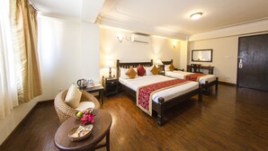 A hotel room with two beds, a wooden floor, a wicker chair, a small table with a basket, and a window with curtains. - Hotel Holy Himalaya (Kathmandu)