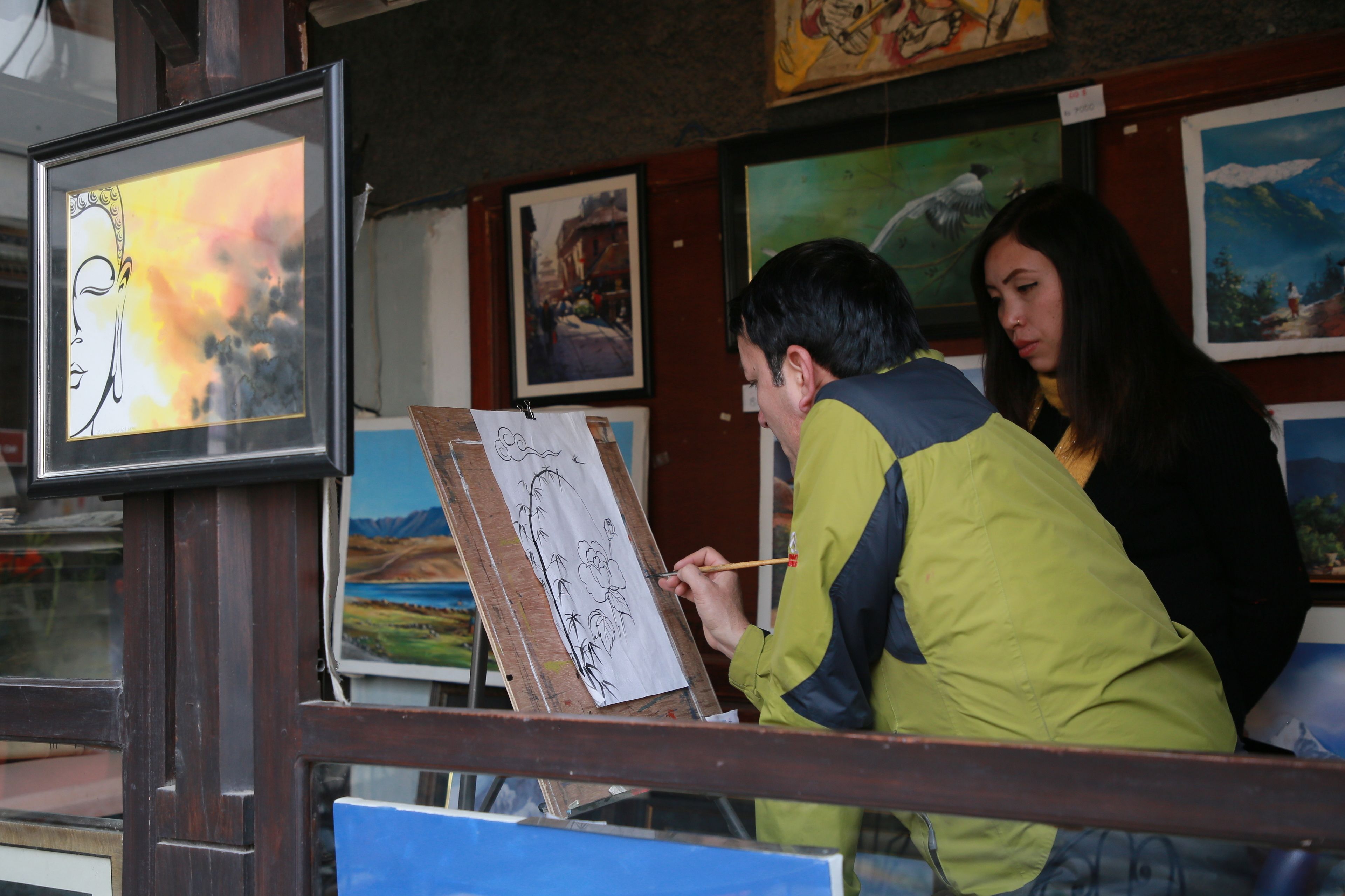 A person painting on a canvas in front of a window.