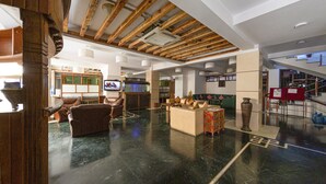 A spacious lobby with a high ceiling, wooden beams, a flat-screen TV, leather seating, and a decorative water feature. - Hotel Holy Himalaya (Kathmandu)
