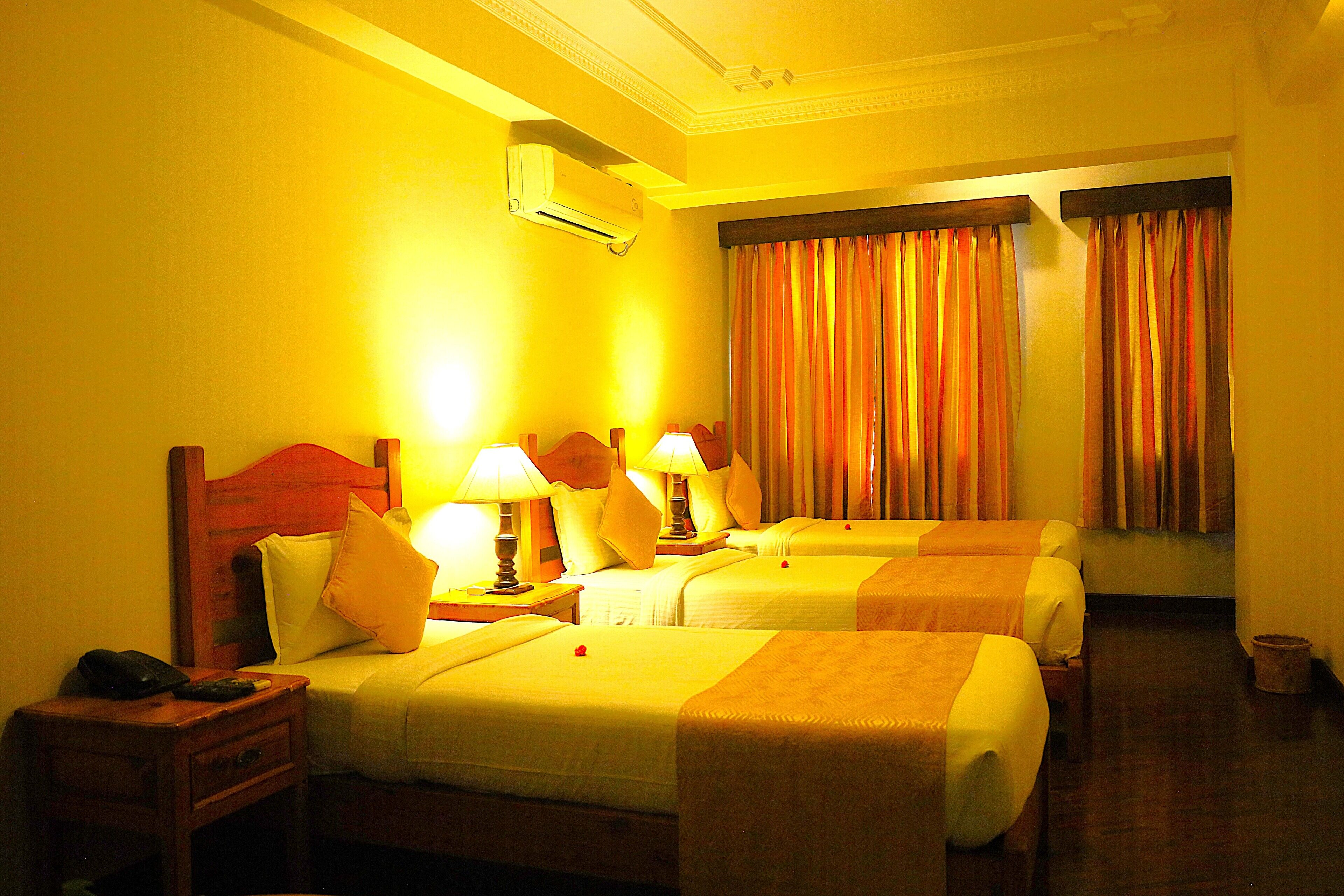 A hotel room with two beds, bedside tables with lamps, a nightstand, and an air conditioning unit.