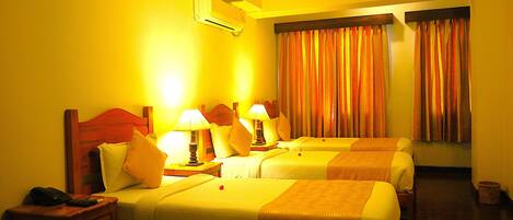 A hotel room with two beds, bedside tables with lamps, a nightstand, and an air conditioning unit.