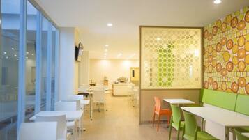 Un comedor moderno con mesas y sillas blancas, una banqueta verde y una pared con diseño.
