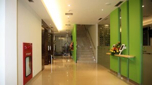 A hotel reception area with a green wall, a reception desk, a staircase, and a hydrant sign. - Zest Bogor by Swiss-Belhotel International (Bogor)