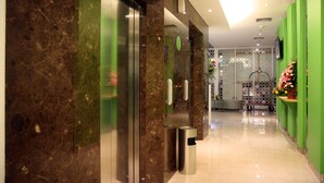 A hotel lobby with a marble reception desk, a green wall, and a glass elevator. - Zest Bogor by Swiss-Belhotel International (Bogor)