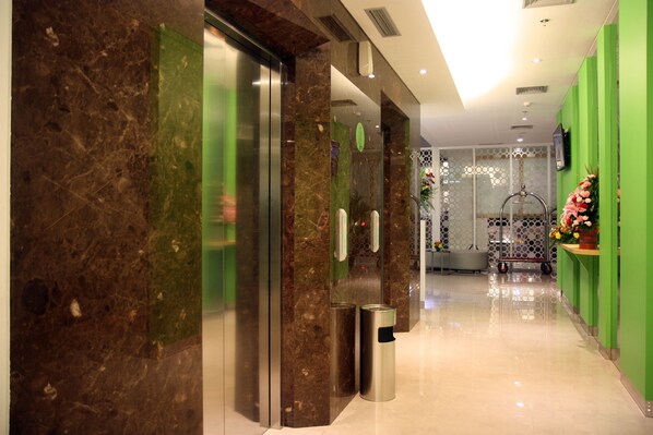 A hotel lobby with a marble reception desk, a green wall, and a glass elevator.