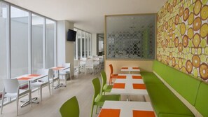 A modern dining area with white and orange tables, green chairs, and a patterned wall. - Zest Bogor by Swiss-Belhotel International (Bogor)