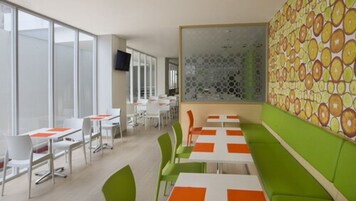 Un comedor moderno con mesas blancas y naranja, sillas verdes y una pared con estampado.