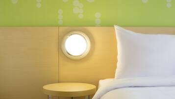 A hotel room with a round mirror on the wall, a small round table, and a neatly made bed with white bedding.