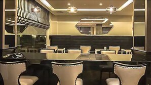Un comedor moderno con una mesa de vidrio rodeada de sillas, un espejo grande e iluminación colgante.