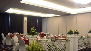 Un salón de conferencias con mesas redondas, sillas blancas y manteles rojos.