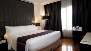 Hotellihuone, jossa on suuri sänky, työpöytä, lamppu ja ikkuna, jossa on verhot.