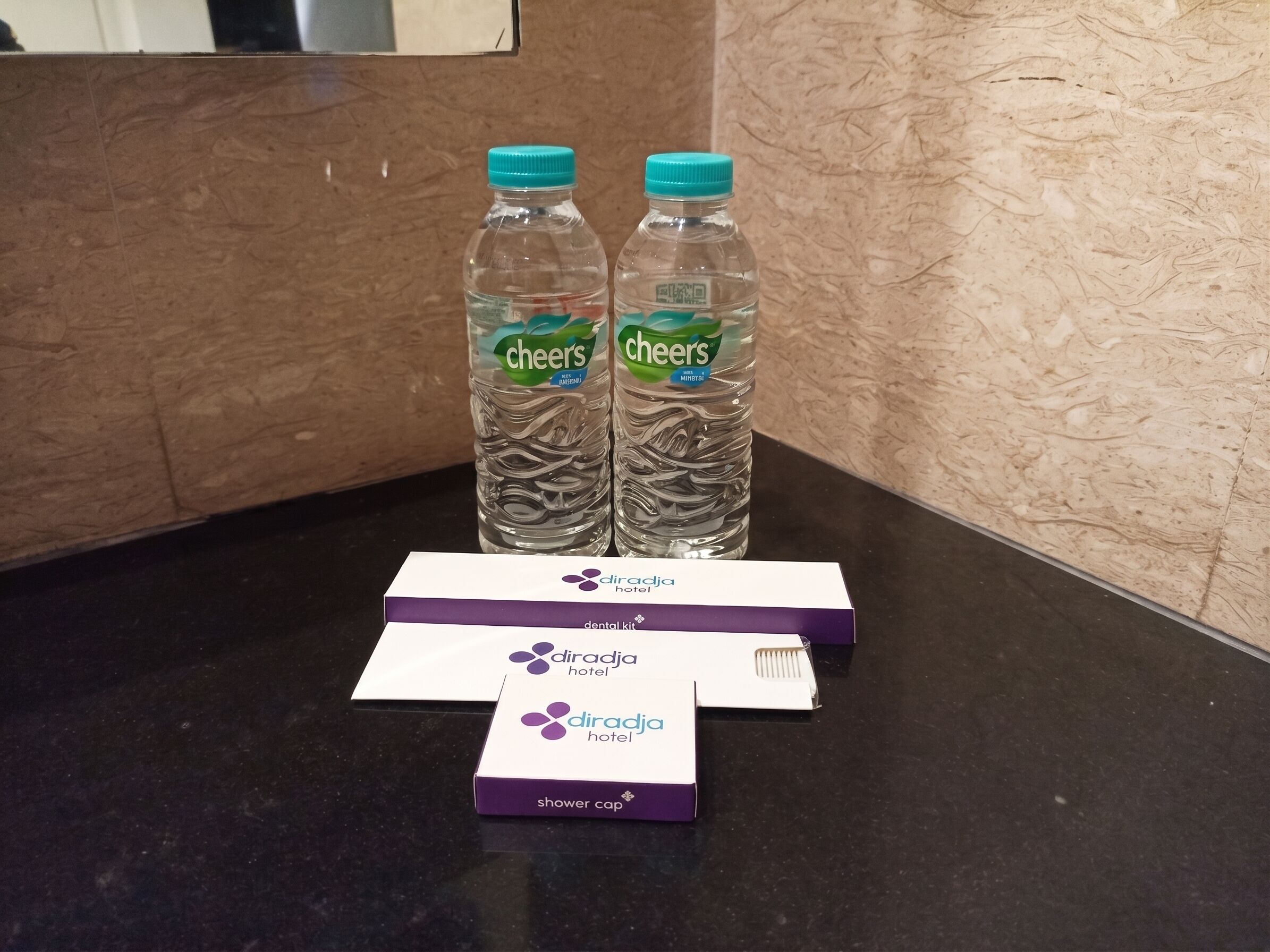 Deux bouteilles d’eau de la marque Cheers, une trousse de soins dentaires et un bonnet de douche, le tout posé sur un comptoir noir.