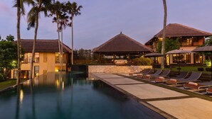 Un resort con piscina, sillas de descanso y construcciones de techo de paja.