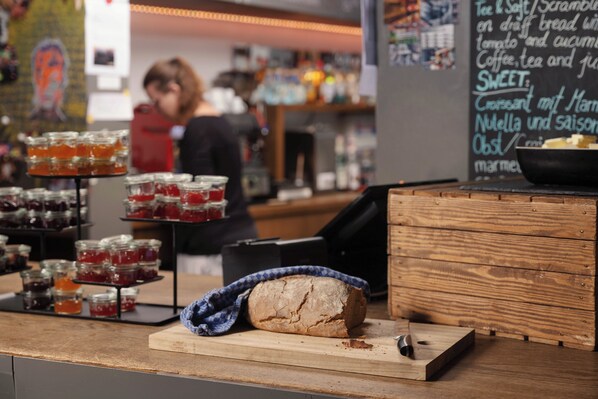 Un comptoir de boulangerie avec des pots de confiture, une miche de pain et, en arrière-plan, un tableau noir servant de menu.