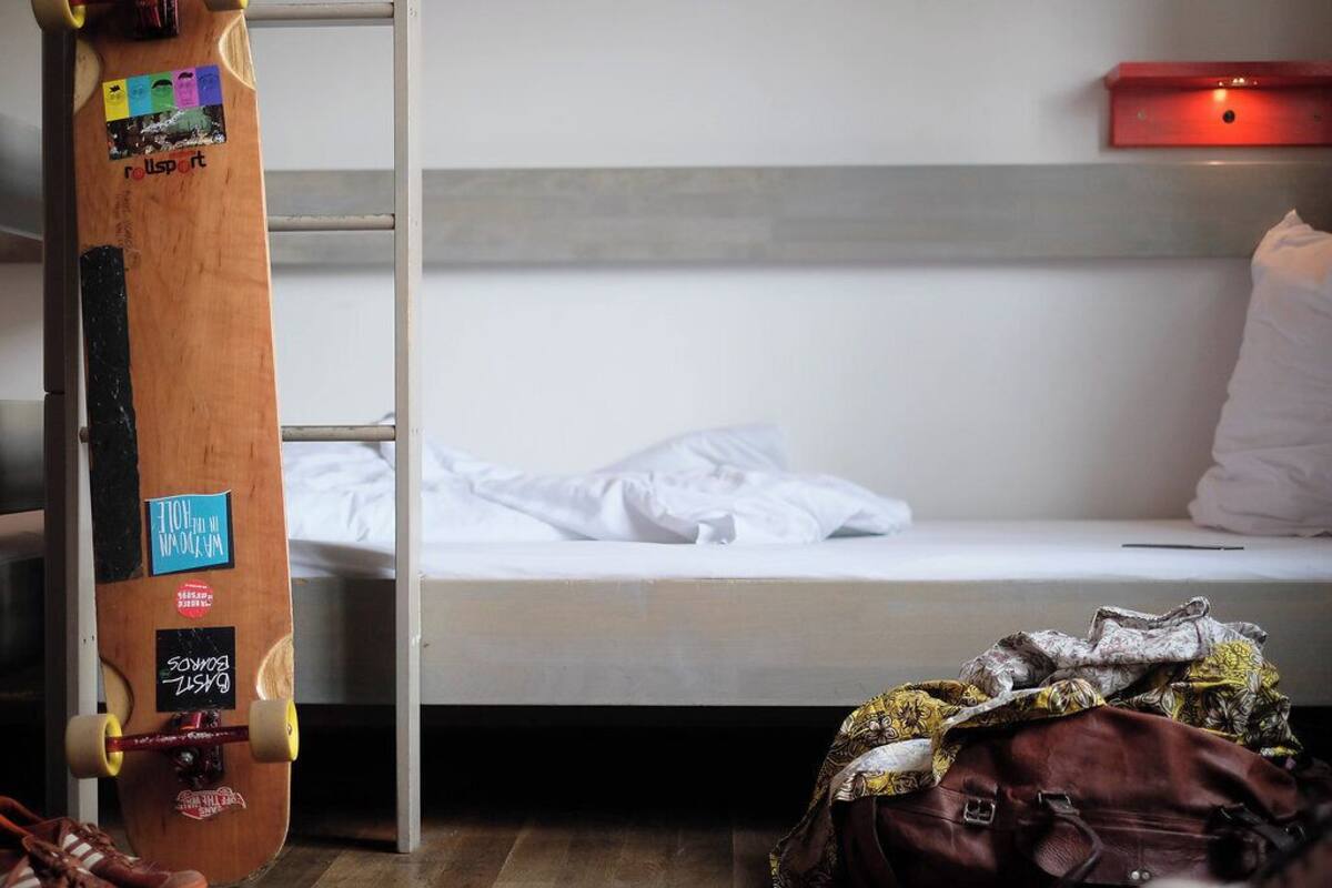 A bunk bed with a wooden ladder, a small red shelf, and a backpack on the floor.