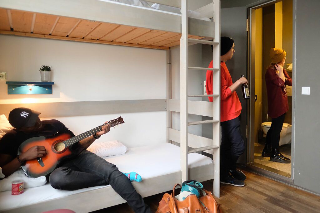 Habitación con literas, una persona tocando la guitarra, otra sosteniendo una botella y un tercero hablando por teléfono.
