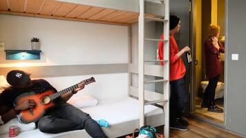 Habitación con literas, una persona tocando la guitarra, otra sosteniendo una botella y un tercero hablando por teléfono.