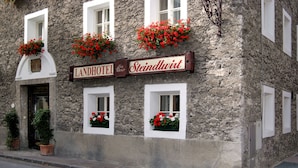 Ein Steinhaus mit einem Schild, auf dem "Landhotel Steindlviert" steht. Über den Fenstern befinden sich Blumenkästen mit roten Blumen.