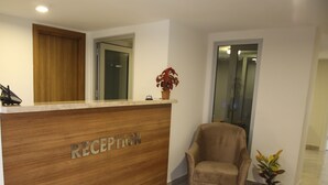 Ein Empfangsbereich mit einem hölzernen Empfangstresen mit der Aufschrift „RECEPTION“, einem komfortablen Sessel und einem Topfpflanzen.