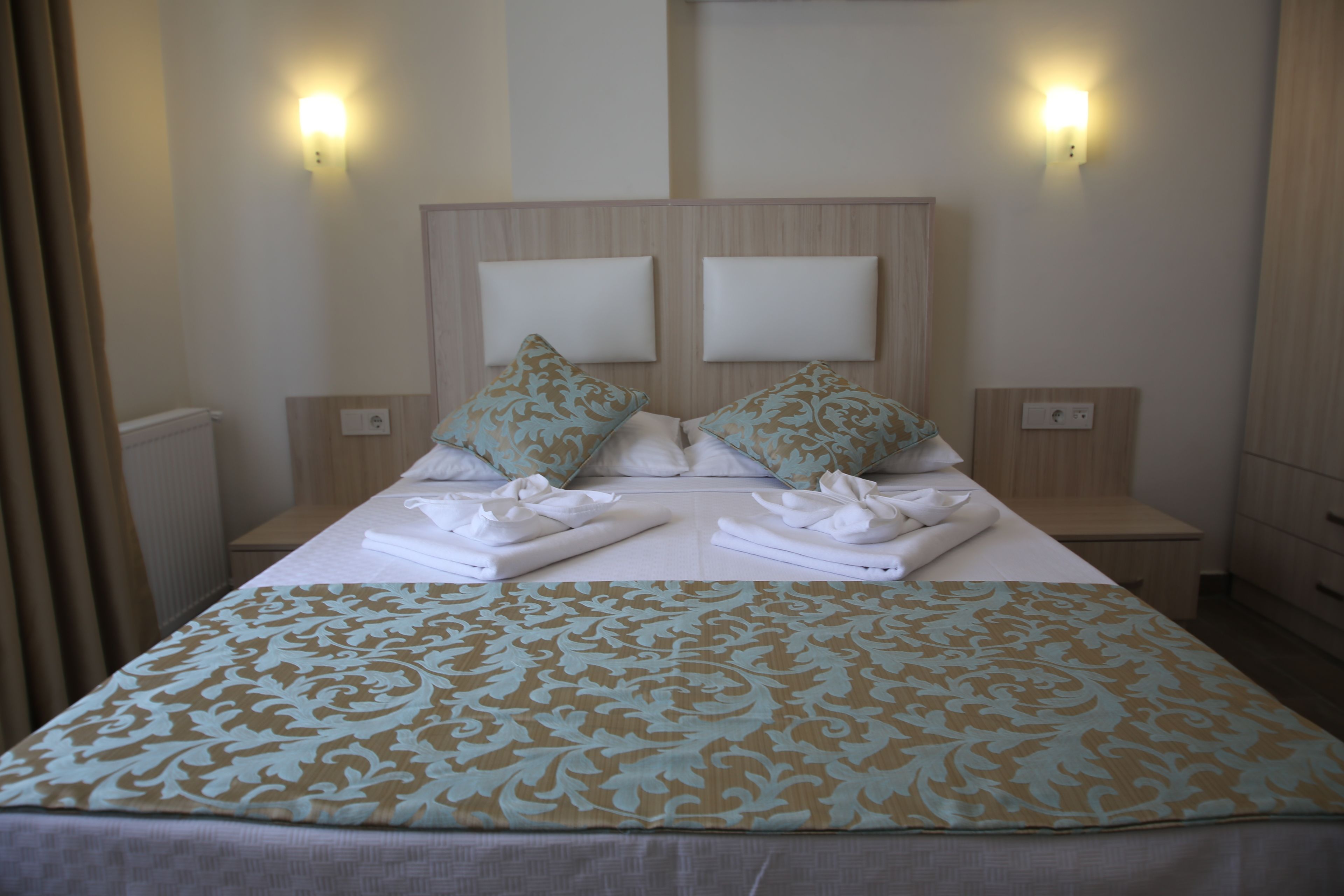 A neatly made bed with a patterned bedspread, two pillows, and a headboard with two light fixtures.