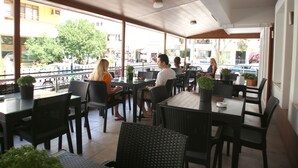 Ein Straßencafé mit Tischen, Stühlen, großen Fenstern und Pflanzkübeln.