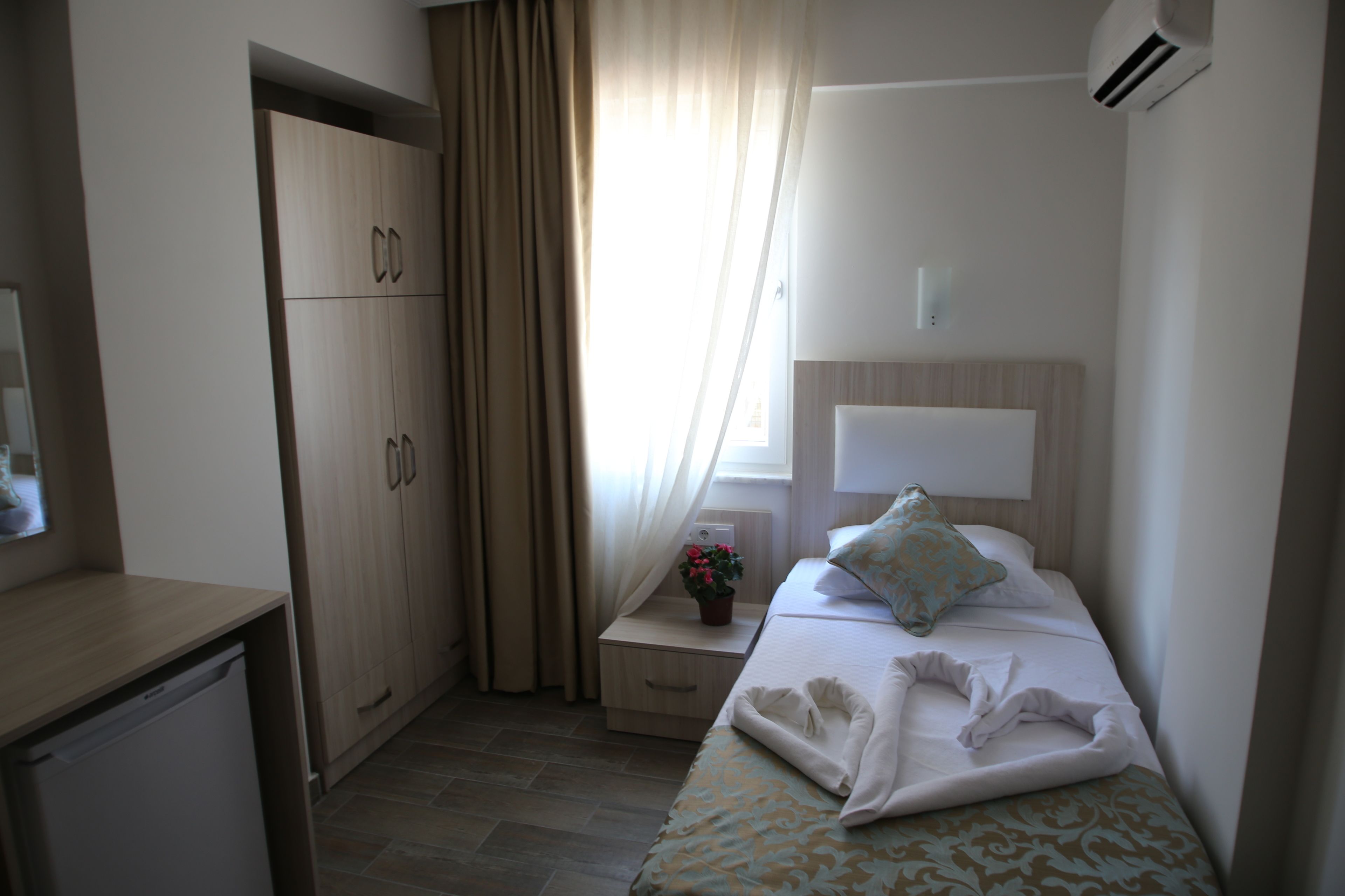 Une chambre d’hôtel avec un lit, une table de chevet avec une lampe, une armoire et une fenêtre avec des rideaux.