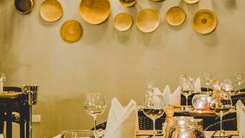 A restaurant interior with a wall of wooden plates and hanging lamps. Tables are set with wine glasses and cutlery.
