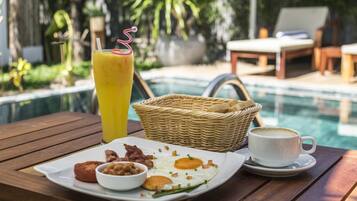 Un desayuno con un plato de huevos, tocino y tostadas, un vaso de zumo de naranja y una taza de café sobre una mesa de madera junto a una piscina.