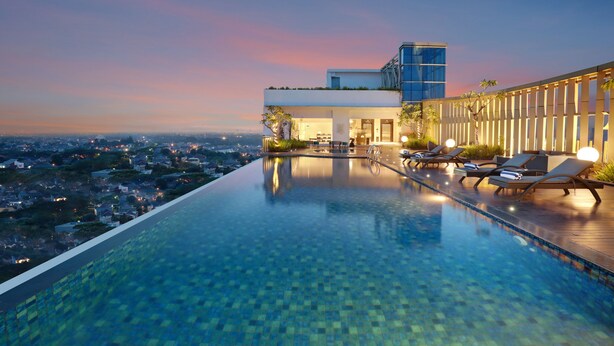 Piscina infinita en la azotea con sillones de descanso y vistas a la ciudad al atardecer.