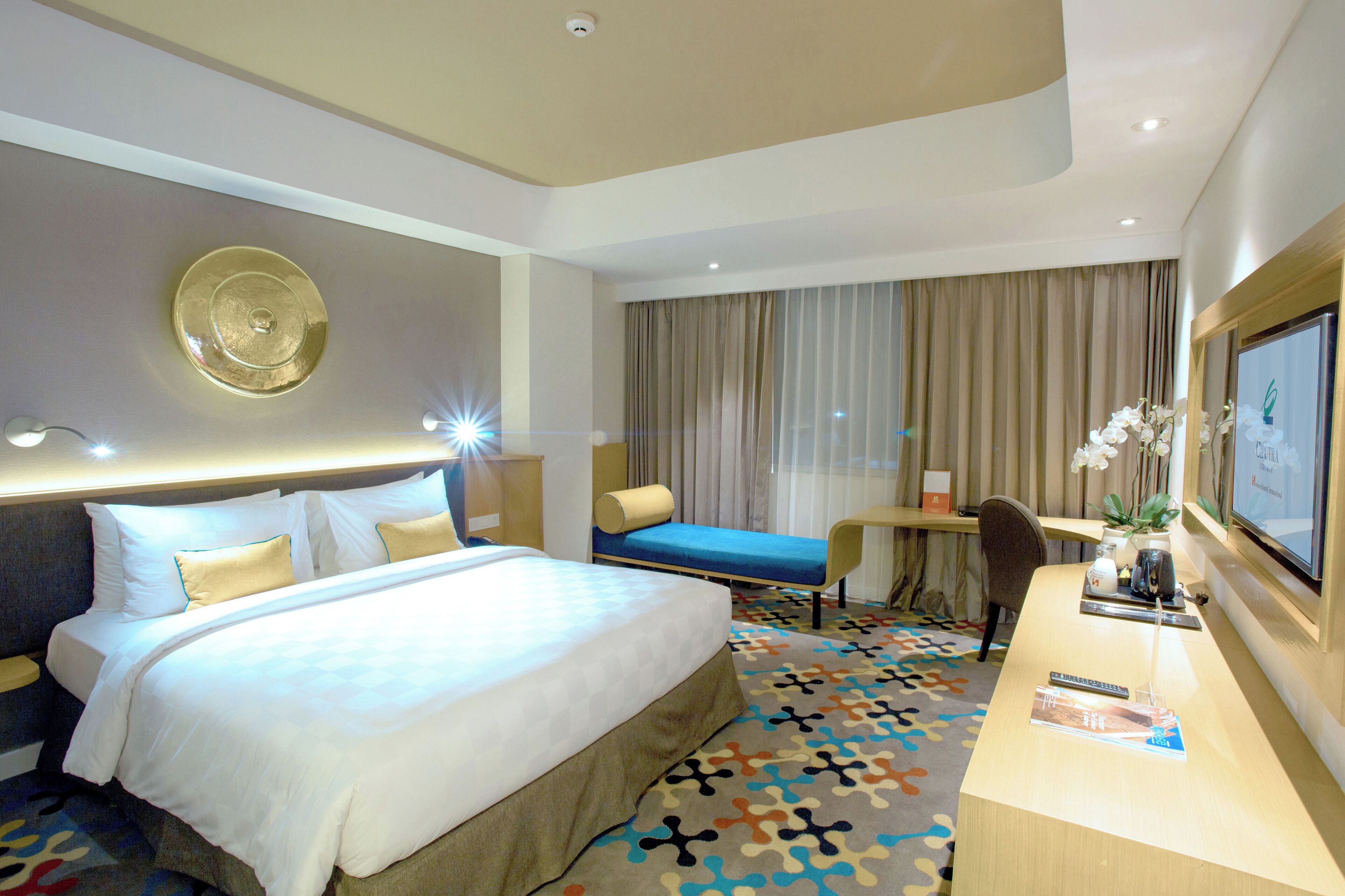 A hotel room with a large bed, a desk, a chair, a television, and a window with curtains.