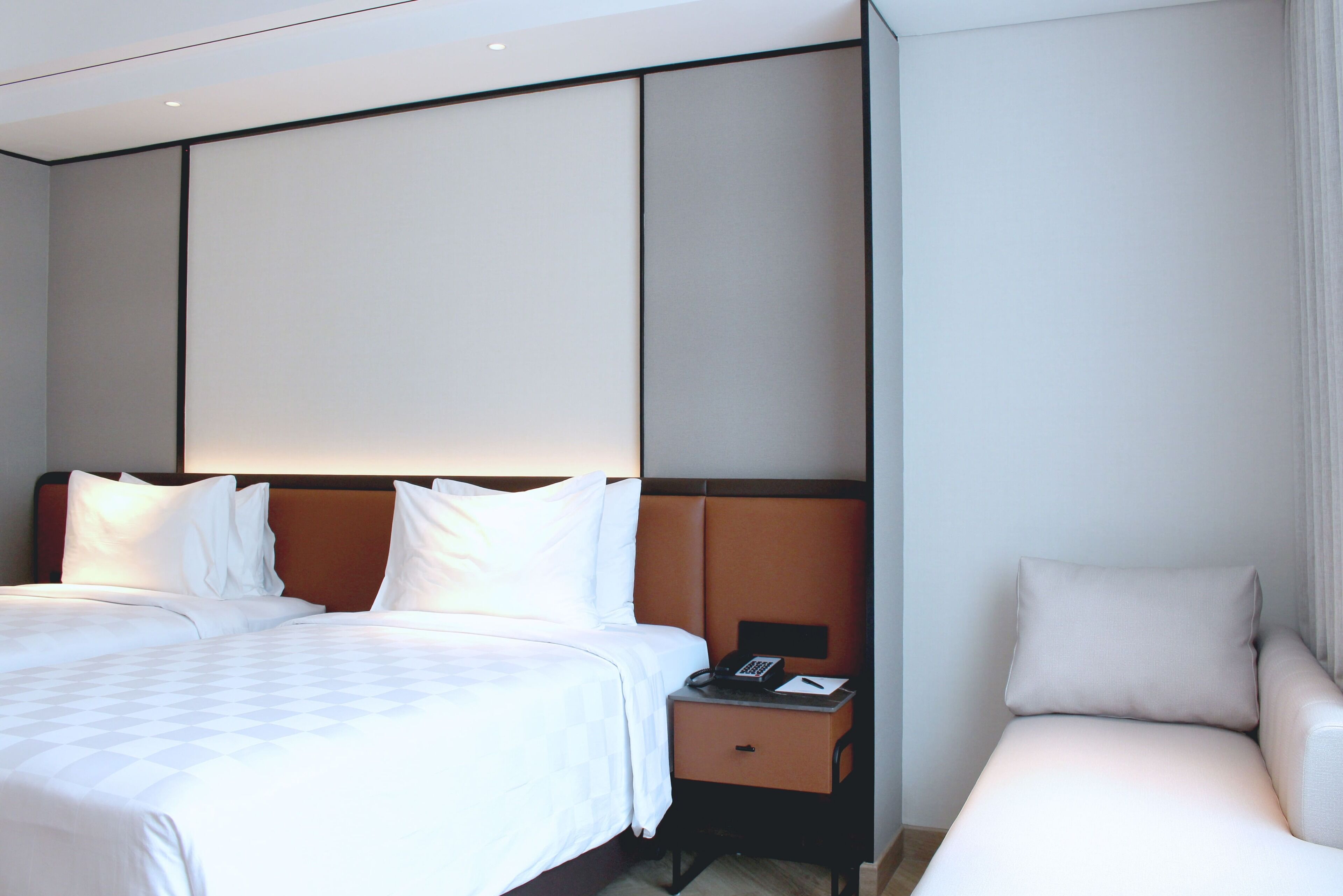 A hotel room with a large bed, a bedside table with a phone, and a sofa.