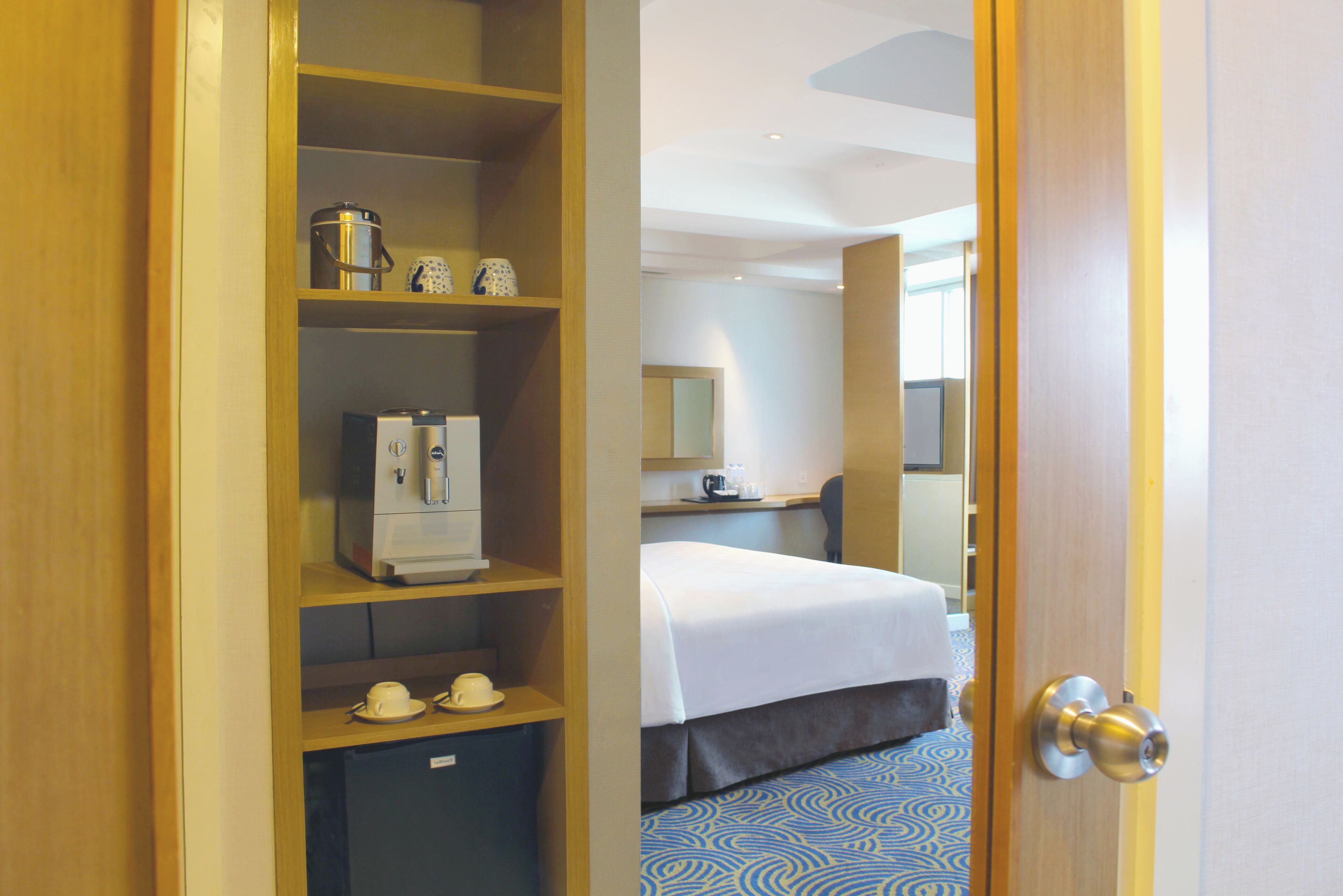 Una camera d'albergo con un letto, una scrivania, una macchina del caffè e un minibar.
