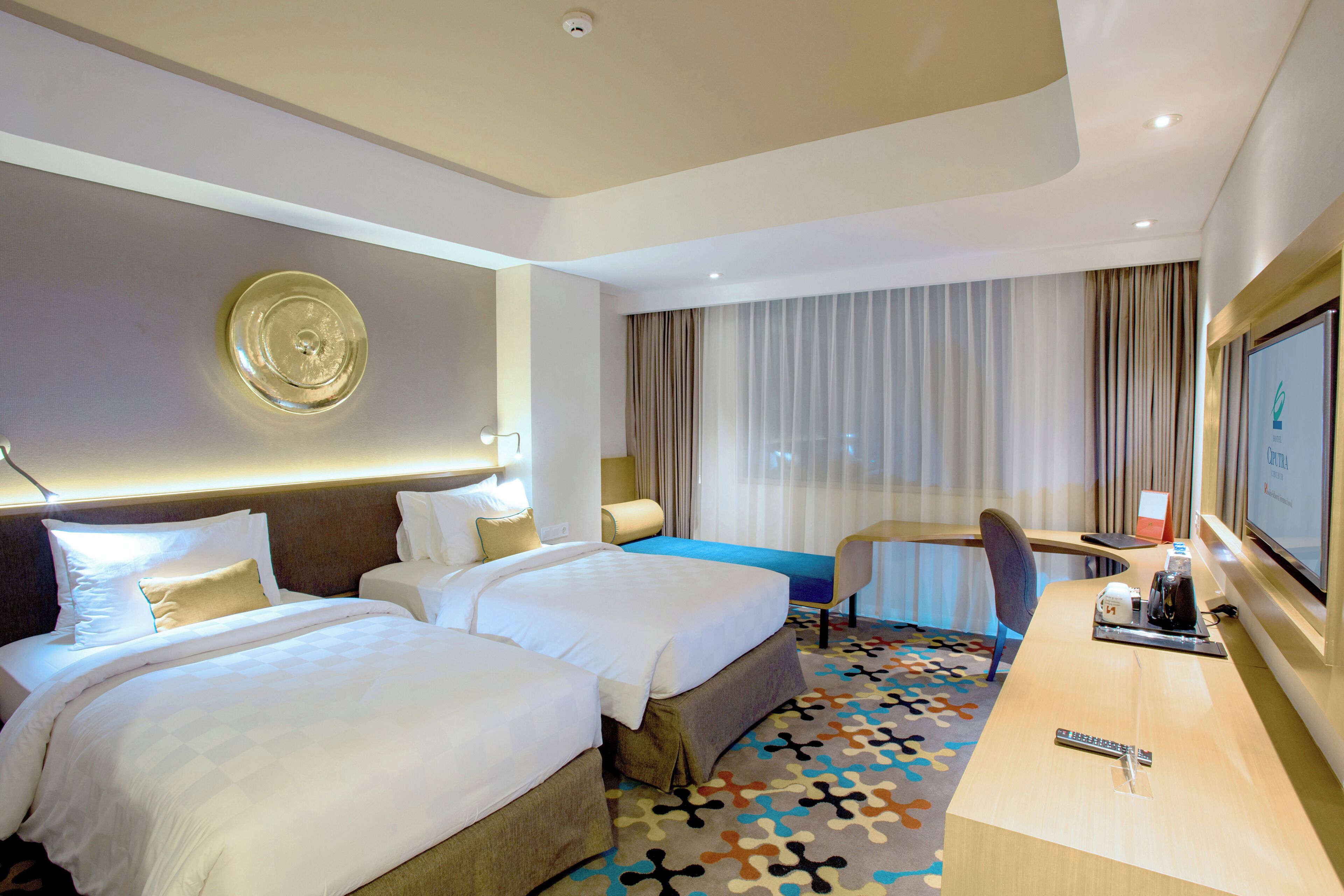 Habitación de hotel con dos camas, un escritorio, una silla, un televisor y una alfombra estampada.