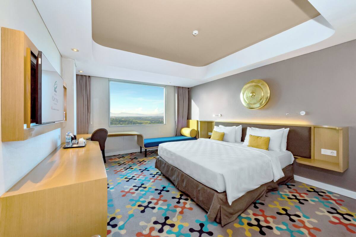A hotel room with a large bed, a desk, a chair, a window with a view, and a decorative wall plate.