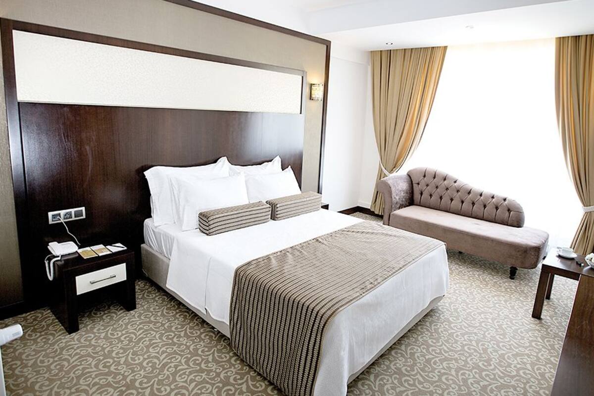 Habitación de hotel con una cama grande, un sofá, una mesita pequeña y una mesita de noche con un teléfono.