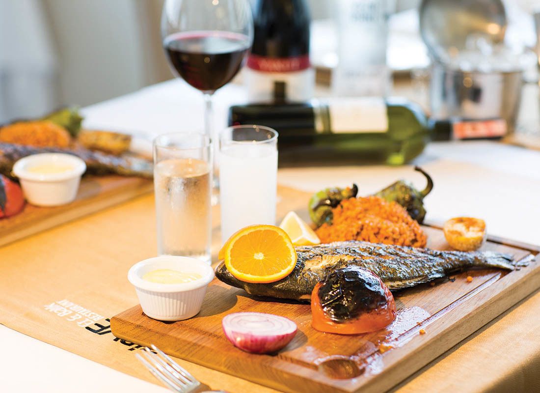 A wooden table with a roasted fish, vegetables, and a glass of red wine.