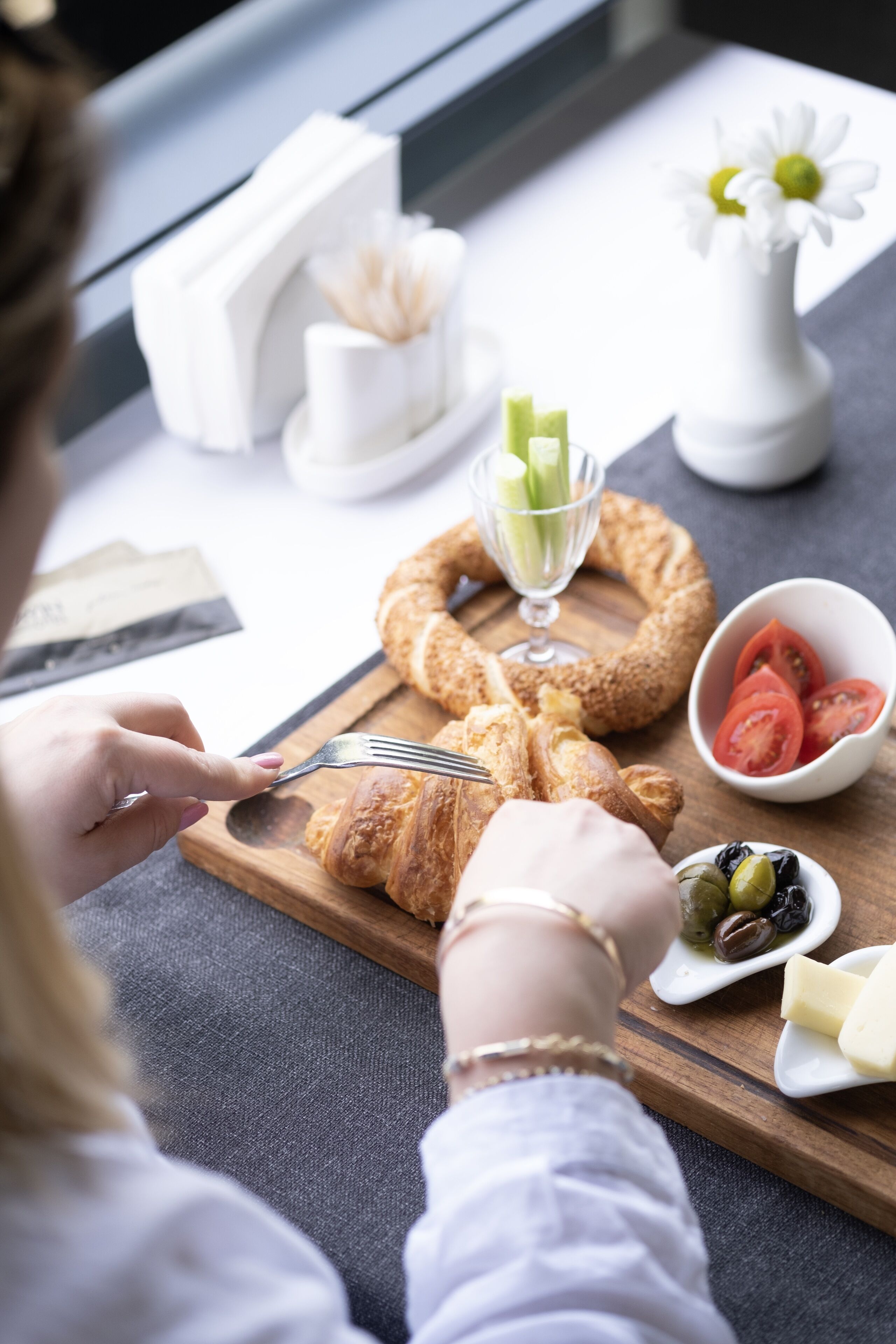 Disposição para o café da manhã com croissants, tomates, azeitonas e queijo em uma tábua de madeira.