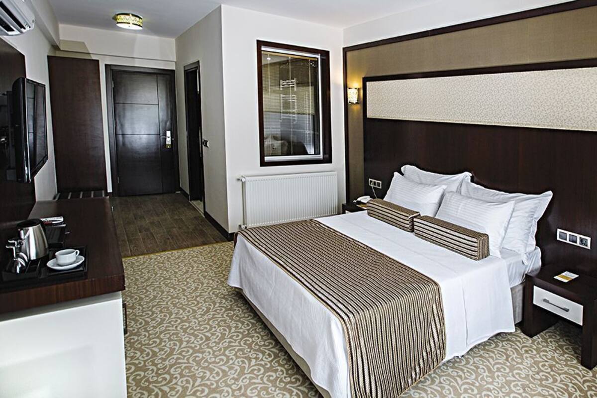 Una habitación de hotel con cama, mesitas de noche, un escritorio con cafetera, televisor y ventana.