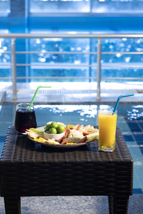 A dining table with a plate of food and drinks, overlooking a pool. - Lavin Otel (Denizli)