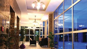 En rymlig entréhall med modern design, utrustad med en sittgrupp, stora fönster och en kristallkrona.