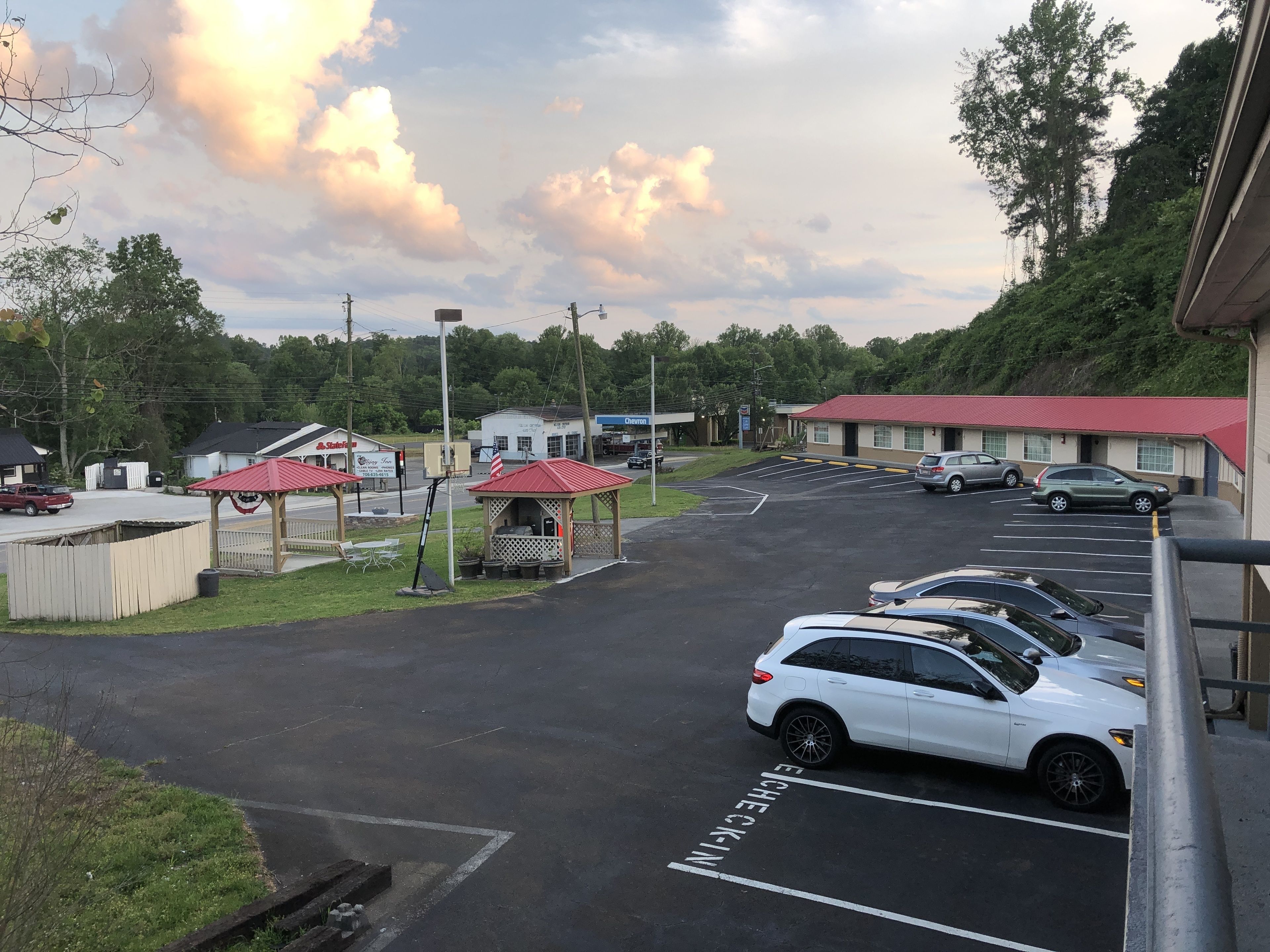 A parking lot with several cars, a gazebo, and a building with a red roof.