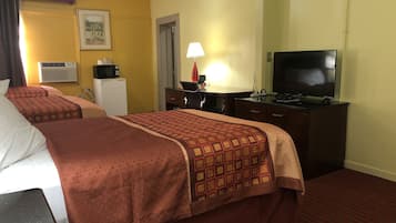 A hotel room with two beds, a TV, a desk, a lamp, and a microwave.