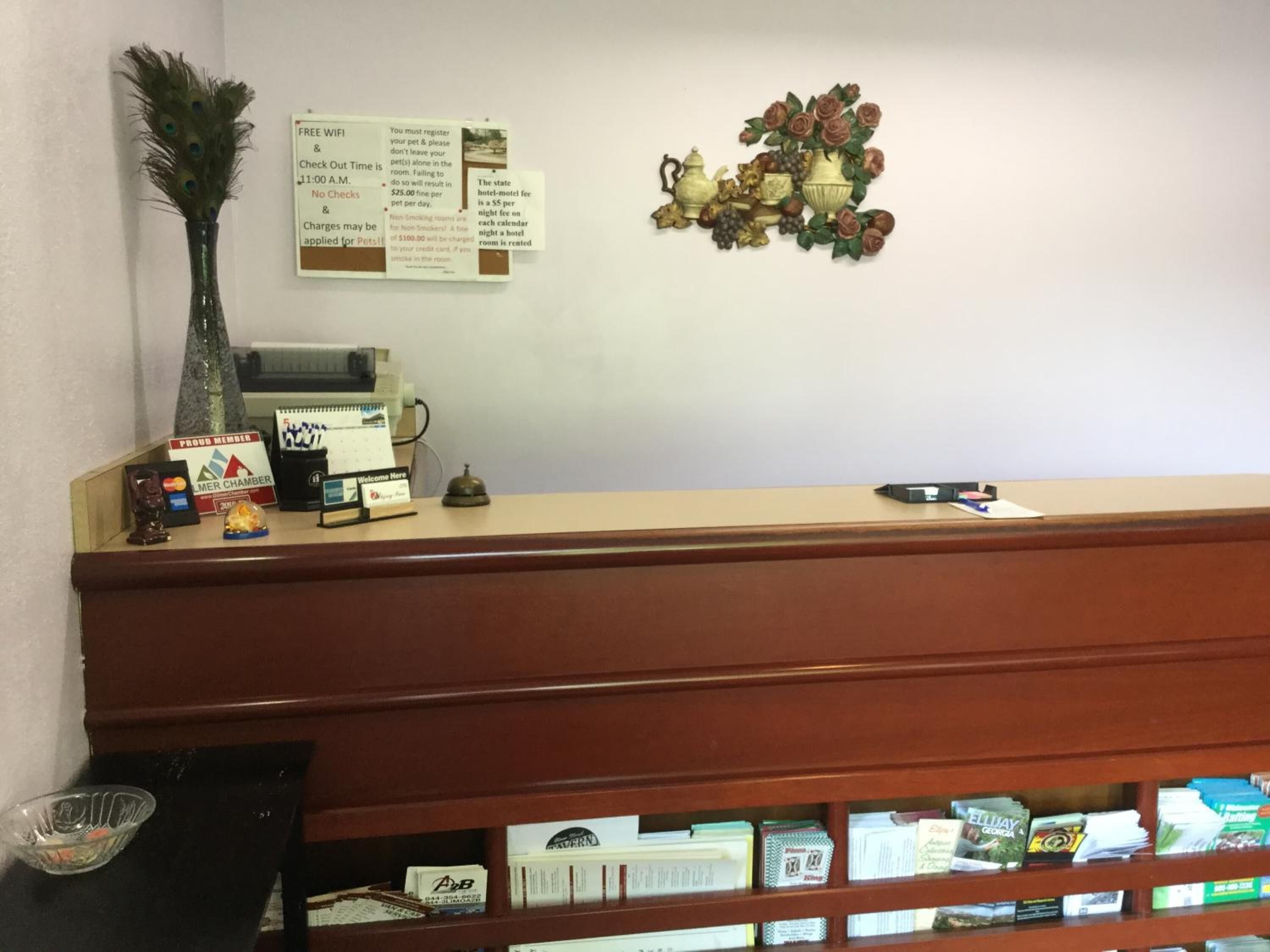 Ein Hotelrezeptionstresen mit Check-in-Schalter, einer wandmontierten Speisekarte und einer dekorativen Blumenkomposition.