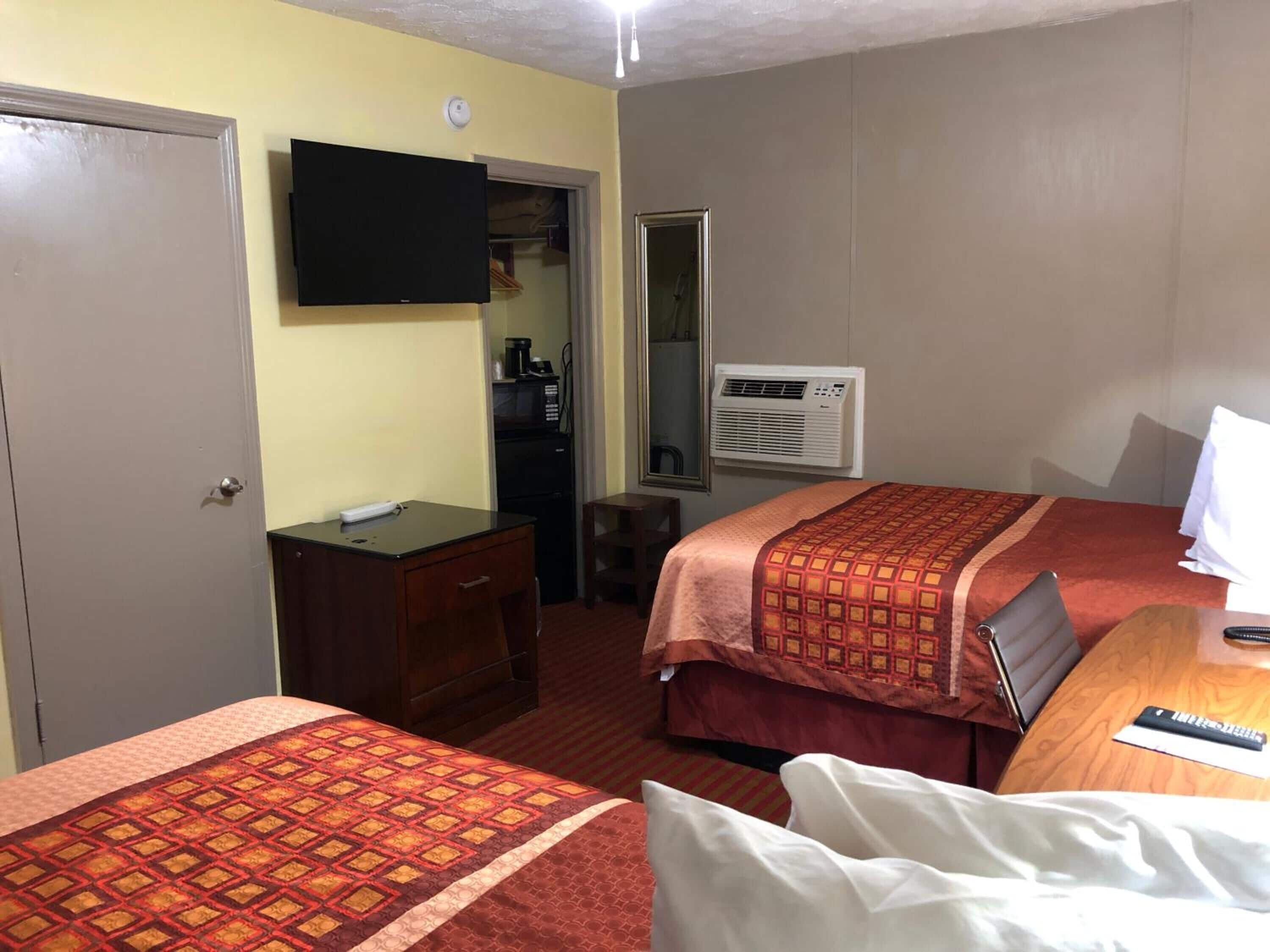 A hotel room with two beds, a desk, a TV, a wardrobe, and an air conditioning unit.