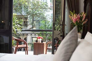 Ein Hotelzimmer mit Balkon, einem Holzbstuhl, einem kleinen Tisch und einer Vase mit Blumen.