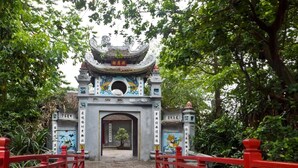Une porte chinoise traditionnelle, ornée de motifs complexes, et un pont rouge qui y mène.